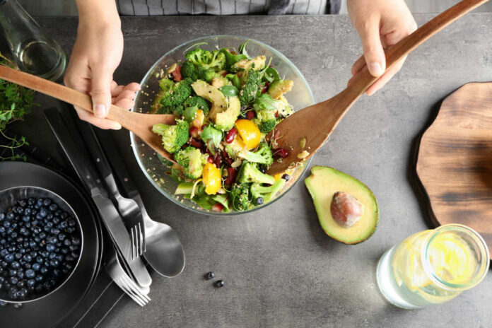 Woman,Mixing,Delicious,Superfood,Salad,Ingredients,With,Wooden,Spoons,In