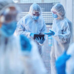 Vaccine Equity Battle: WHO’s New Plan Healthcare workers in protective gear discussing information on a tablet outdoors