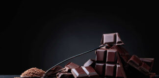 A pile of dark chocolate bars with cocoa powder on a black surface