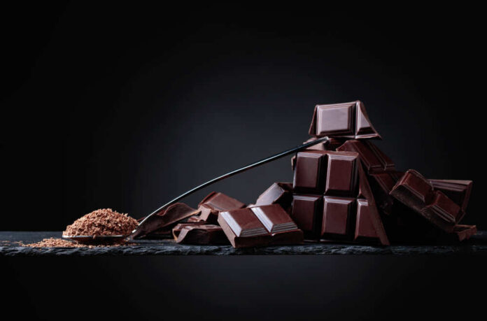 shutterstock_1105033433.jpg A pile of dark chocolate bars with cocoa powder on a black surface