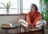 A relaxed woman sitting in a chair with a smile, surrounded by plants and natural light