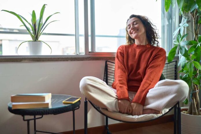 A relaxed woman sitting in a chair with a smile, surrounded by plants and natural light