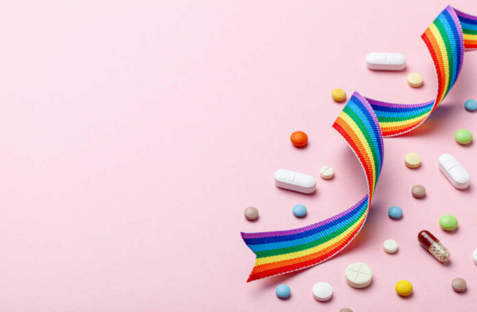 Colorful pills and a rainbow ribbon on a pink background