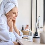 WRONG Problem: Dark Spots Not Your Real Enemy Woman in a bathrobe with a towel on her head, smiling at her reflection in a mirror