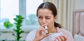 Woman applying nasal spray while holding a tissue in a cozy indoor environment