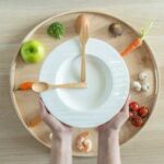 Hands holding a white plate surrounded by fresh vegetables and an egg