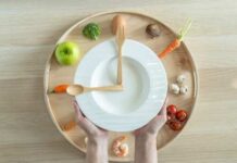 Hands holding a white plate surrounded by fresh vegetables and an egg